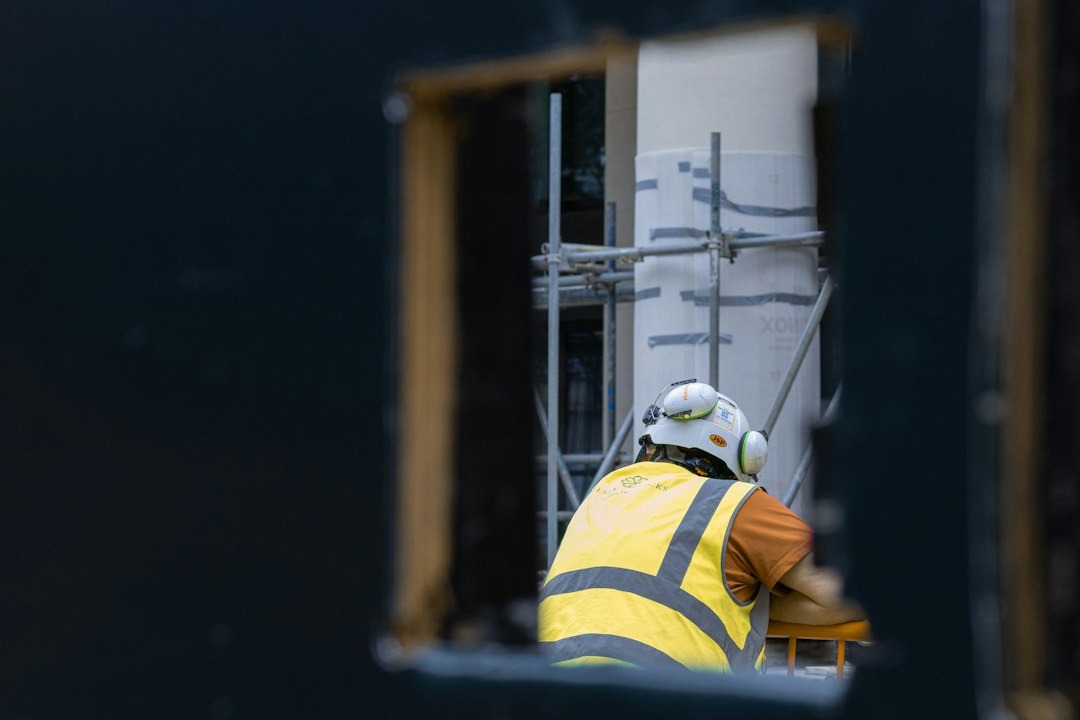A worker in a hard hat and high-visibility vest seen through an opening in a wall