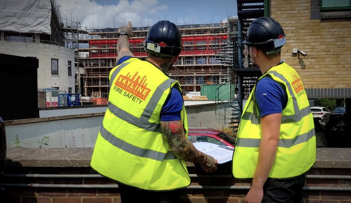 Two fire safety workers in high-visibility vests observing a construction site outdoors.