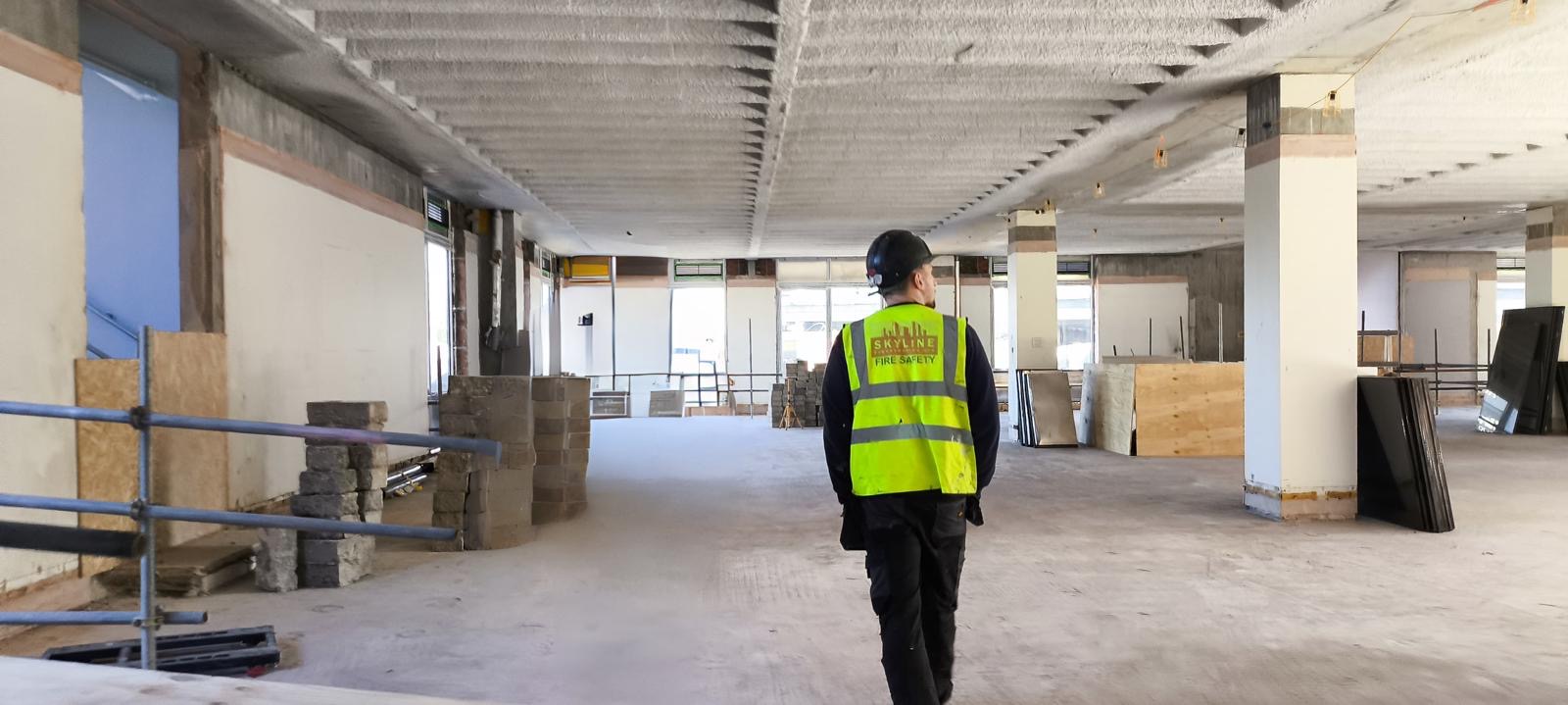 Worker in high-visibility vest walks through building interior under construction.