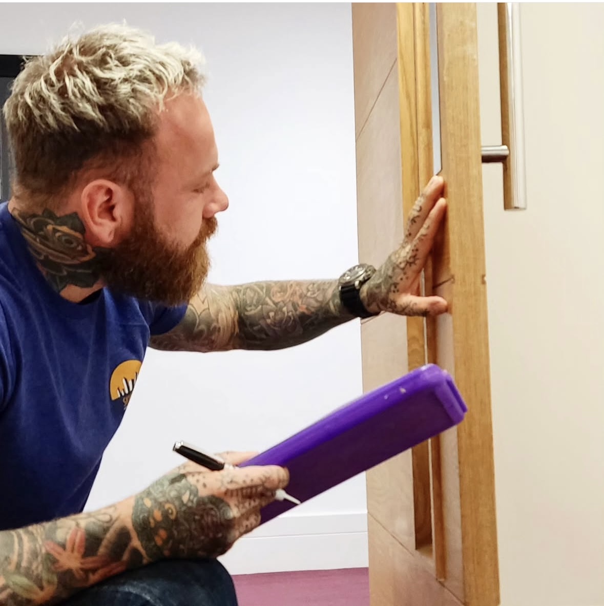 Technician with clipboard and pen inspects a wooden door frame during building assessment.