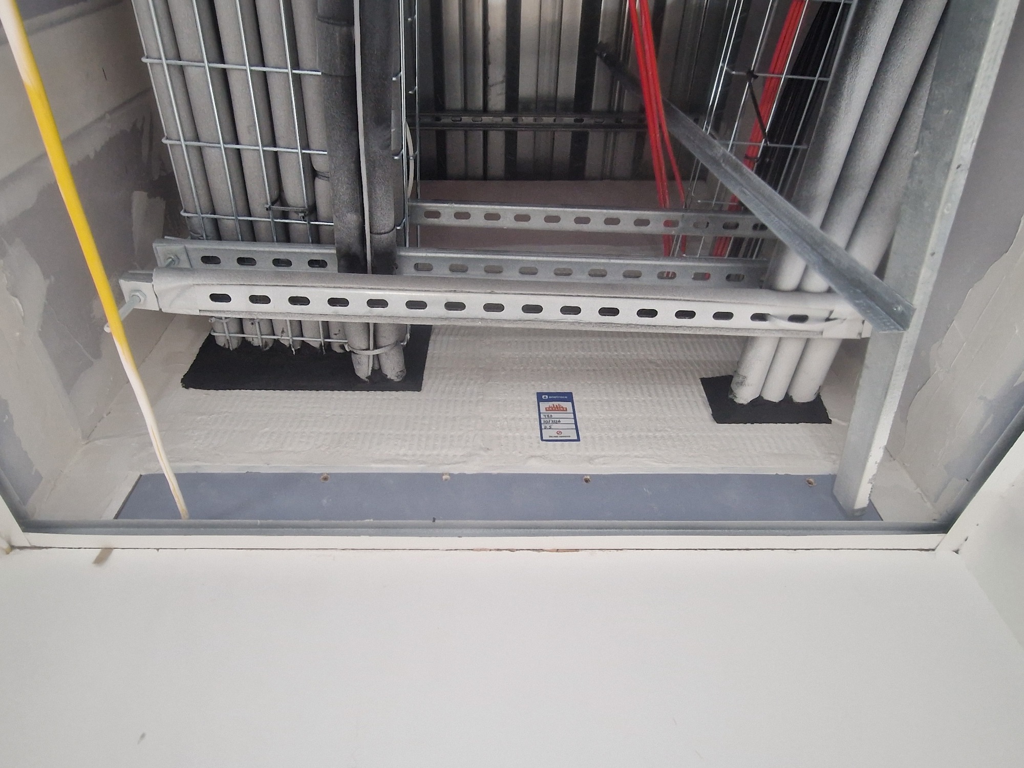 Service shaft with cable trays and pipe penetrations through a fire-rated floor assembly.