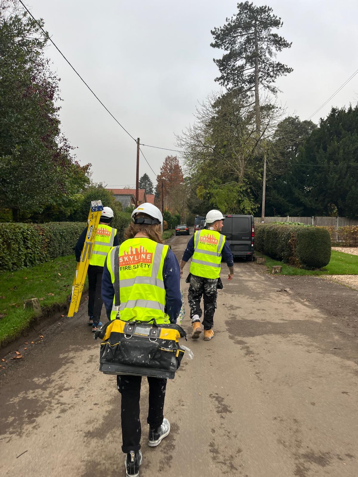 Three operatives in high-visibility vests and hard hats walking along a lane carrying equipment