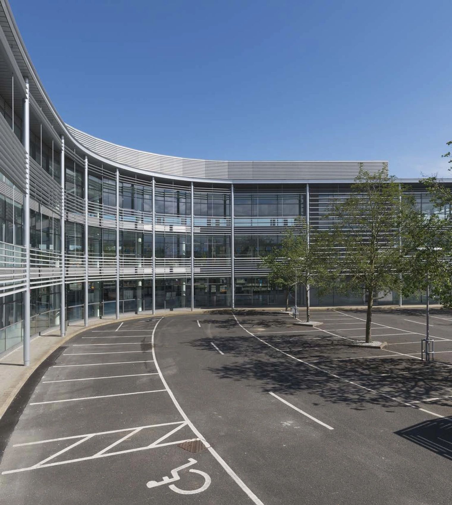 A completed curved glass building beside an empty car park