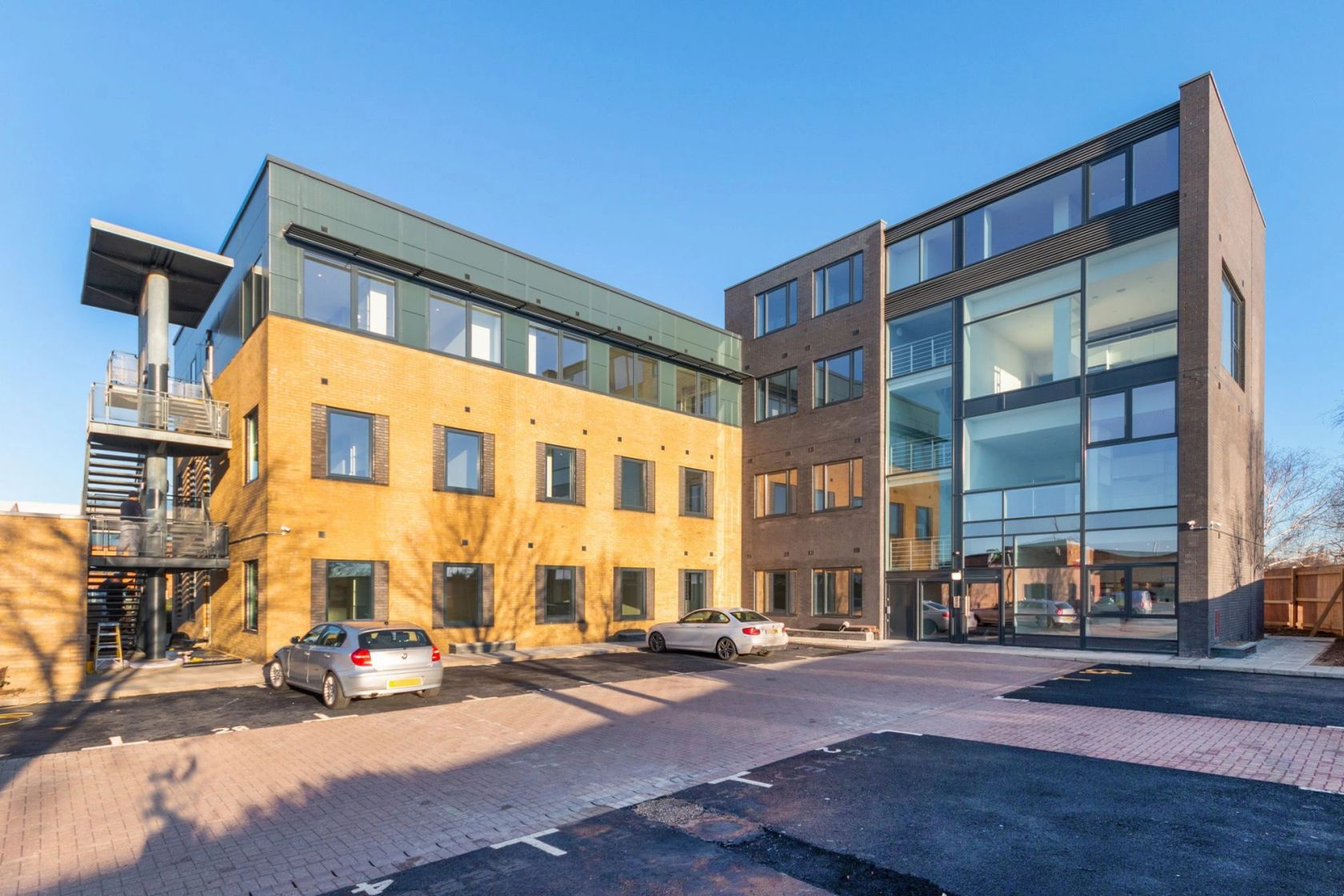 Modern mixed-use building with brick and glass facade and parking area.