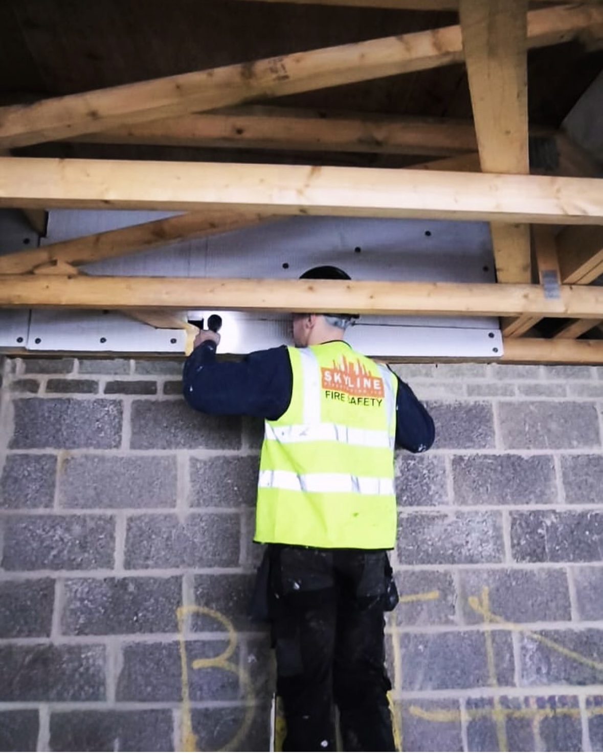 Operative in a high-visibility vest working at the head of a blockwork wall below timber joists