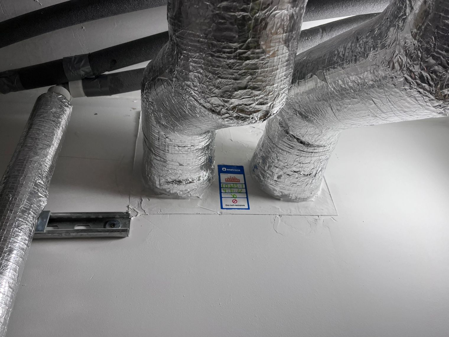 Insulated pipes wrapped in foil passing through a sealed fire-rated wall penetration.