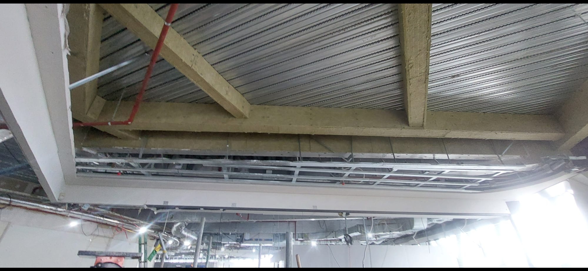 View looking up at exposed ceiling cavity showing concrete beams, metal decking, and suspended ceiling grid framework.